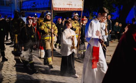 Na obrazku widać procesję, na początku idzie dwóch duchownych, za nimi strażacy niosący baldachim