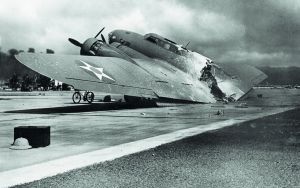 Zniszczony B-17 na lotnisku Hickam Field. W tle po lewej widoczne dymy pożarów fot. Wikipedia / domena publiczna